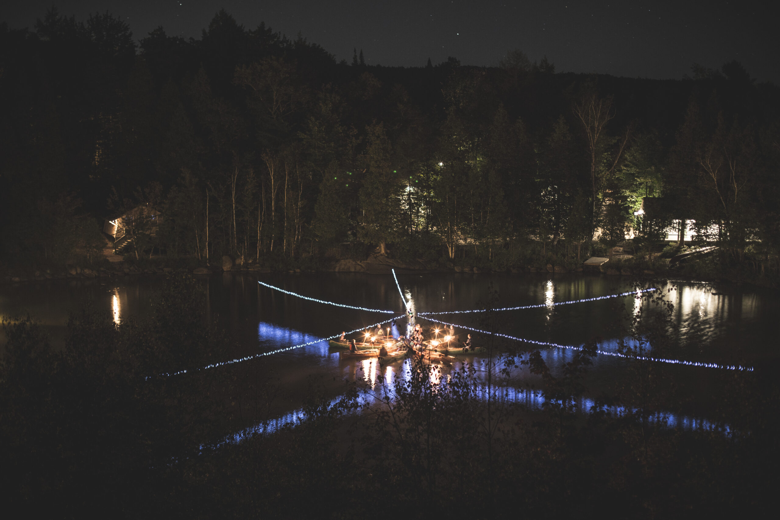 des adeptes du canoe sont rassemblé de nuit sur leurs canots formant une étoile et chaque personne ayant une torche sur son canot